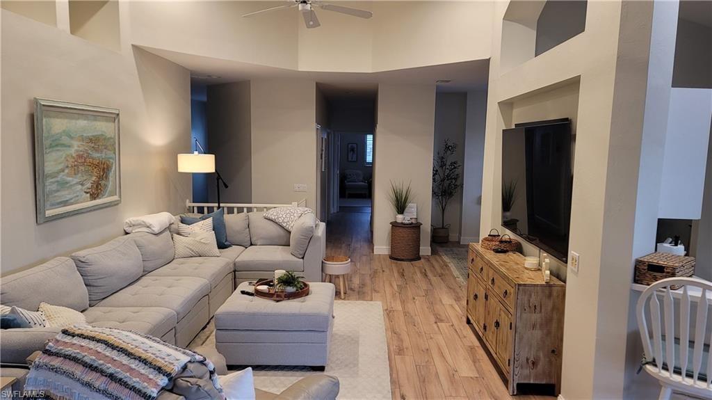 Living area featuring light wood-style floors, a ceiling fan, and a high ceiling