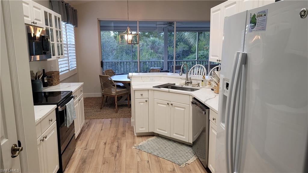 Kitchen with stainless steel appliances, a peninsula, decorative light fixtures, light wood-type flooring, and plenty of natural light
