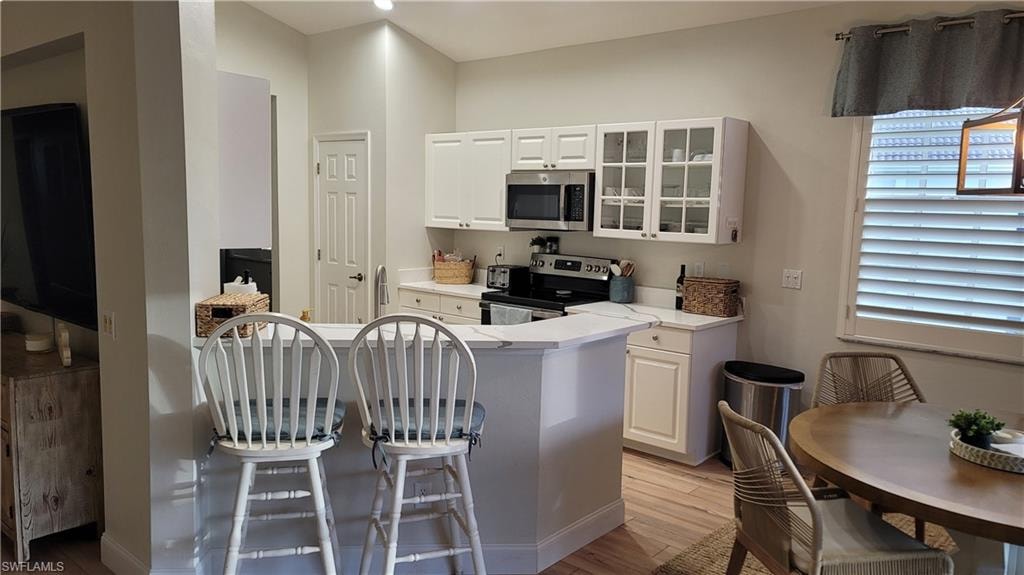 Kitchen with light countertops, stainless steel appliances, a kitchen breakfast bar, and white cabinetry