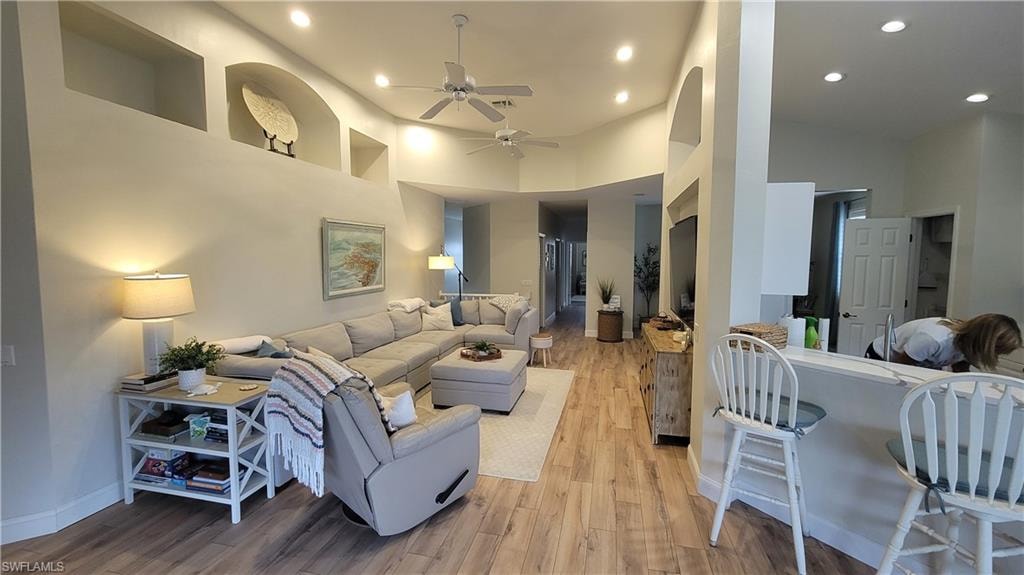 Living room featuring light wood-style floors, a high ceiling, recessed lighting, and a ceiling fan