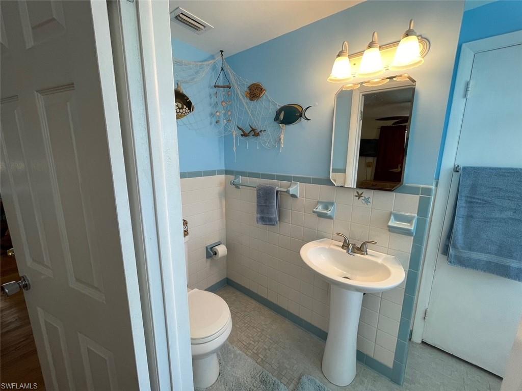 Bathroom featuring a wainscoted wall, toilet, tile walls, and visible vents