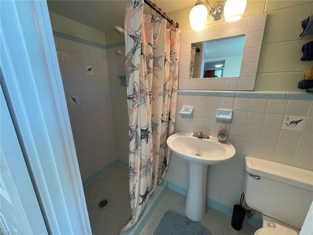 Full bath featuring tile patterned floors, toilet, tile walls, and a stall shower