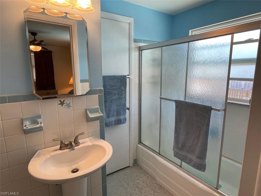 Full bathroom with shower / bath combination with glass door, tile walls, ceiling fan, and a sink