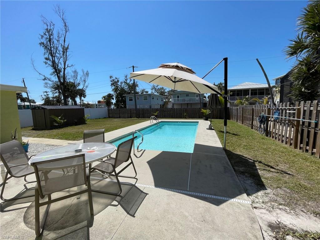 View of swimming pool with outdoor dining space, a patio, a fenced backyard, a storage unit, and a lawn