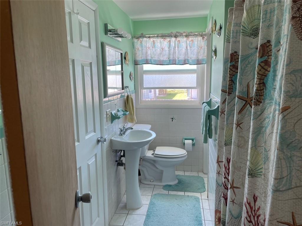 Bathroom with a shower with shower curtain, tile patterned flooring, wainscoting, tile walls, and toilet