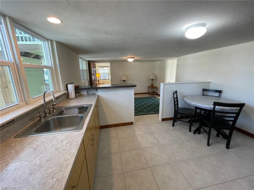 Kitchen with baseboards, light tile patterned floors, a peninsula, a textured ceiling, and a sink