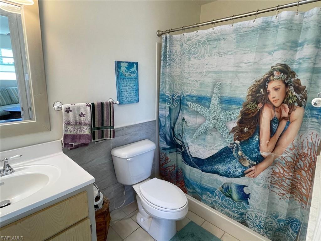 Full bathroom featuring vanity, wainscoting, tile patterned floors, toilet, and tile walls