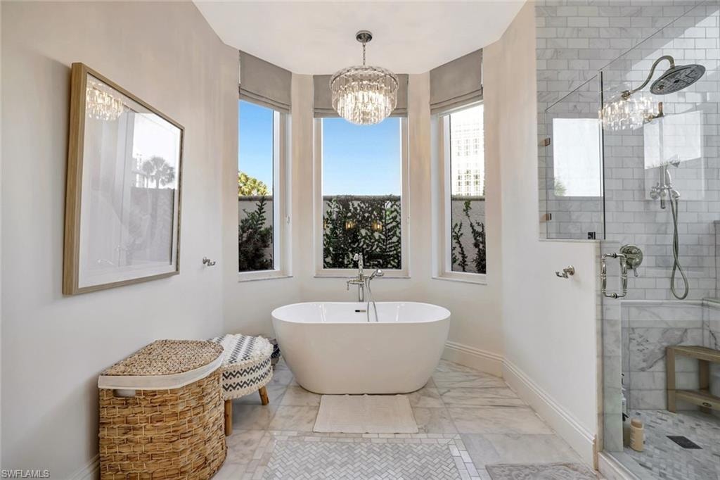 Bathroom featuring a stall shower, a freestanding tub, large windows and a chandelier