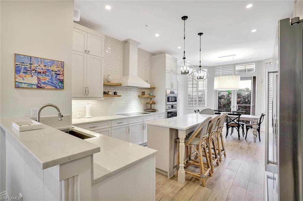 Large kitchen featuring a center island, a kitchen breakfast bar, a wine cellar, stainless steel appliances, light stone countertops, and light wood-style floors