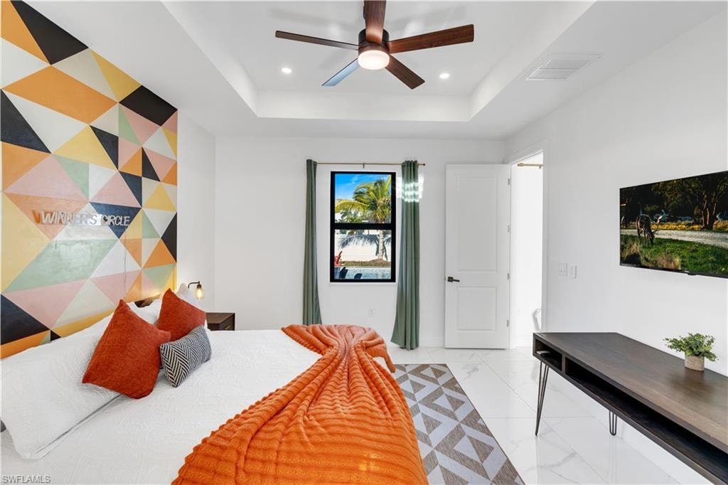 Bedroom featuring an accent wall, a tray ceiling, ceiling fan, recessed lighting, and light marble finish flooring