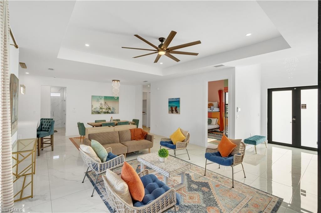Living area with a raised ceiling, a ceiling fan, recessed lighting, french doors, and light marble finish floors