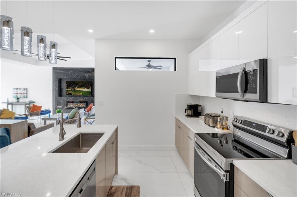 Kitchen with stainless steel appliances, modern cabinets, hanging light fixtures, light stone counters, and open floor plan