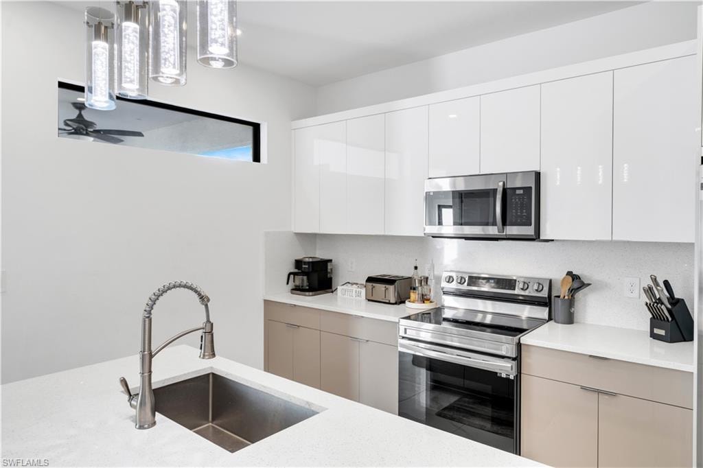 Kitchen featuring modern cabinets, stainless steel appliances, white cabinetry, light stone countertops, and pendant lighting
