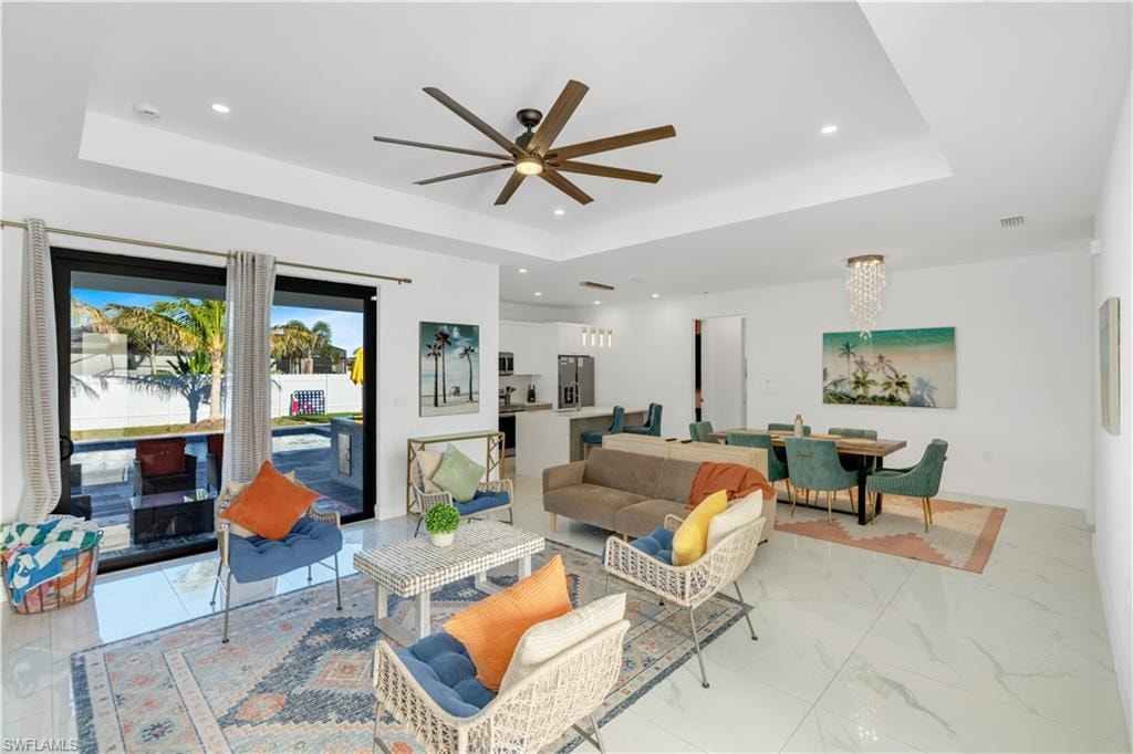 Living room with a ceiling fan, recessed lighting, a raised ceiling, a chandelier, and light marble finish floors