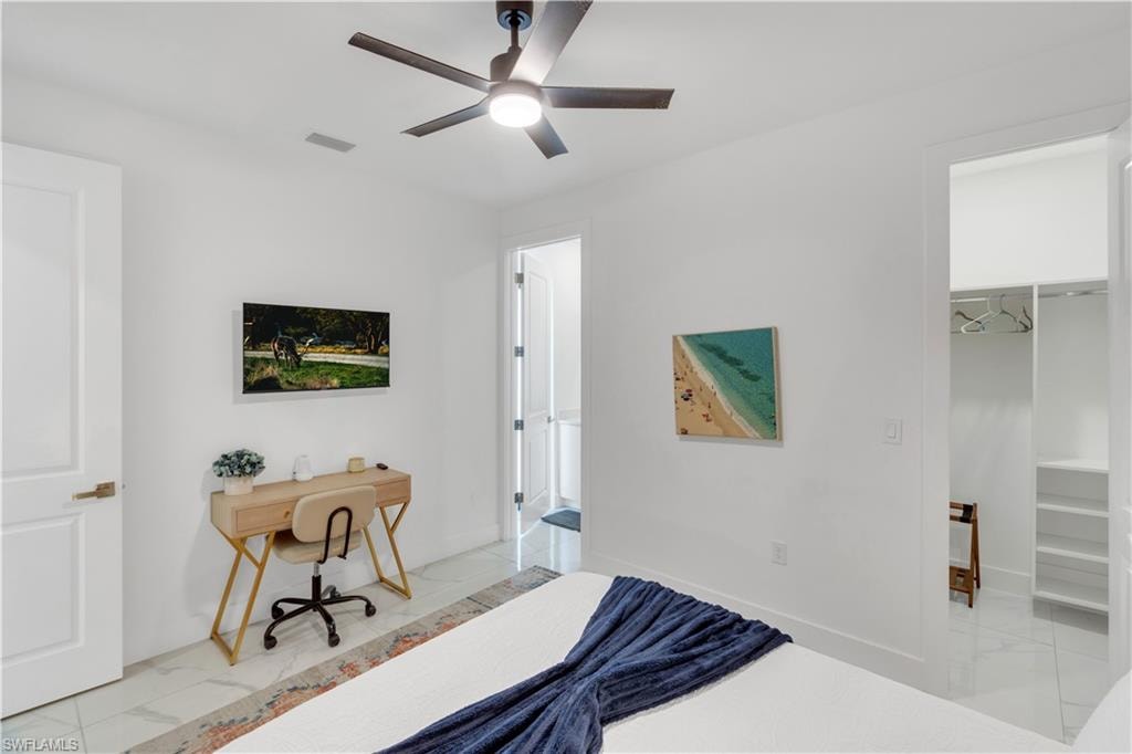 Bedroom featuring light marble finish floors, a desk, a spacious closet, and a ceiling fan