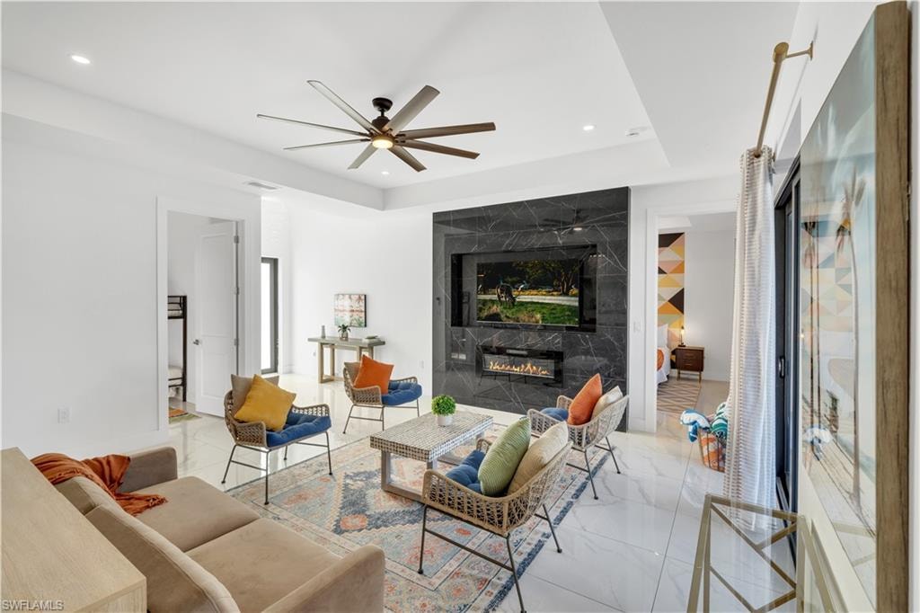 Living room with a high end fireplace, a tray ceiling, a ceiling fan, recessed lighting, and an accent wall
