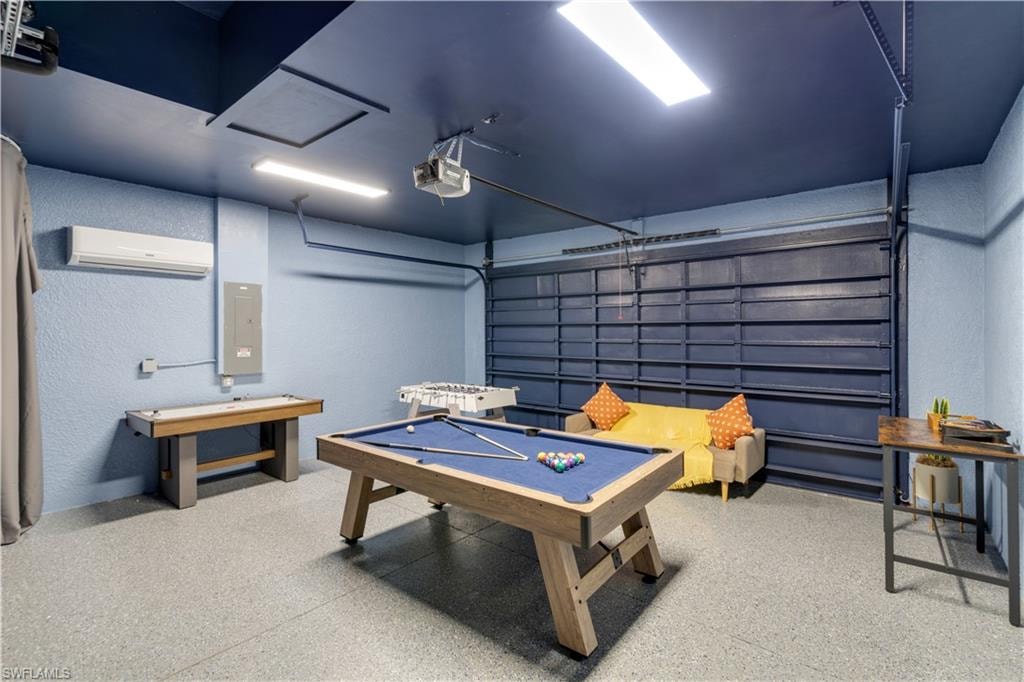 Recreation room with a textured wall, a garage, pool table, electric panel, and dark speckled floor