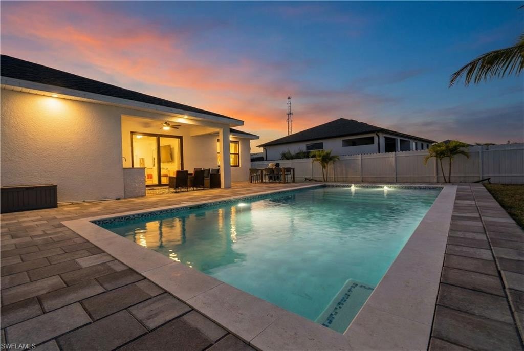 Pool at dusk with a patio area, a fenced backyard, and outdoor dining area