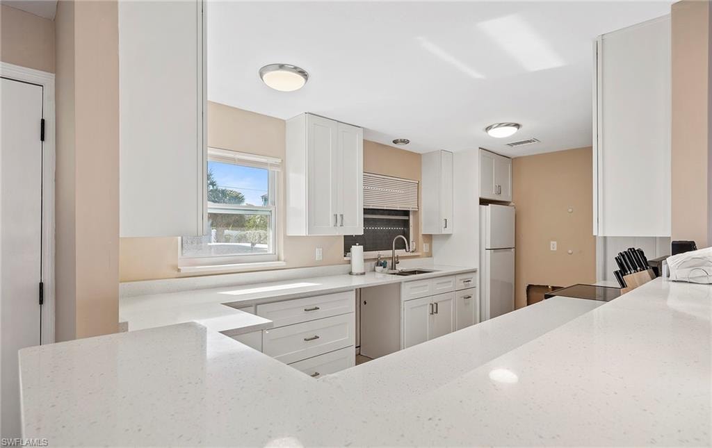 Kitchen with white fridge, sink, white cabinets, and light stone counters