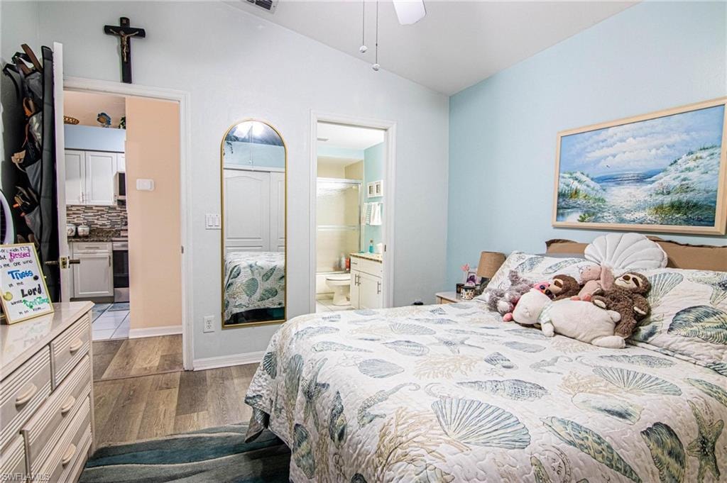 Bedroom with ensuite bathroom, vaulted ceiling, ceiling fan, and light hardwood / wood-style floors