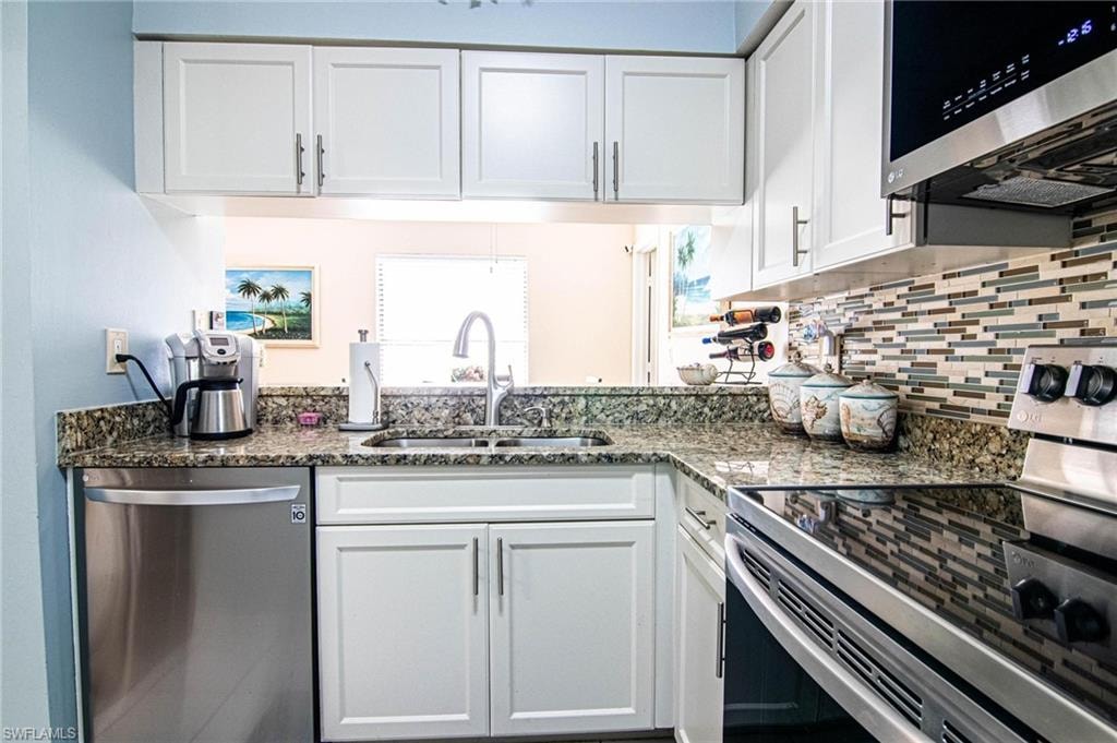 Kitchen with appliances with stainless steel finishes, backsplash, dark stone counters, sink, and white cabinetry
