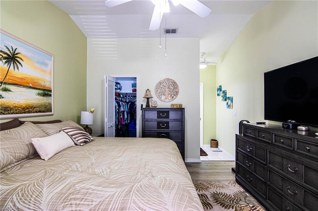 Bedroom with ceiling fan, a spacious closet, light hardwood / wood-style floors, lofted ceiling, and a closet