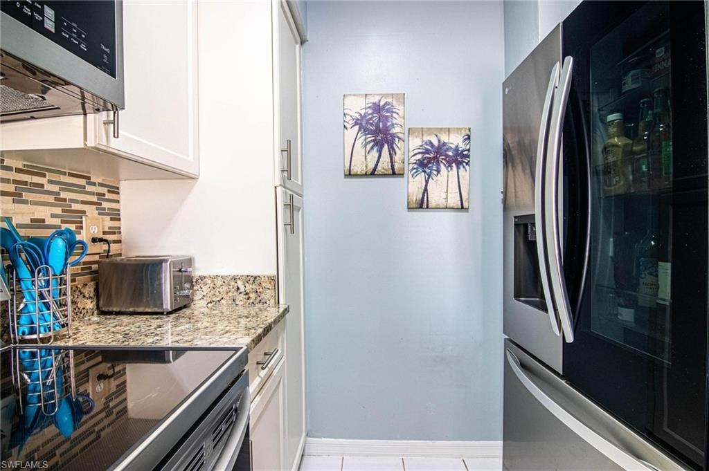 Kitchen featuring backsplash, light stone counters, stainless steel fridge with ice dispenser, white cabinetry, and light tile patterned flooring