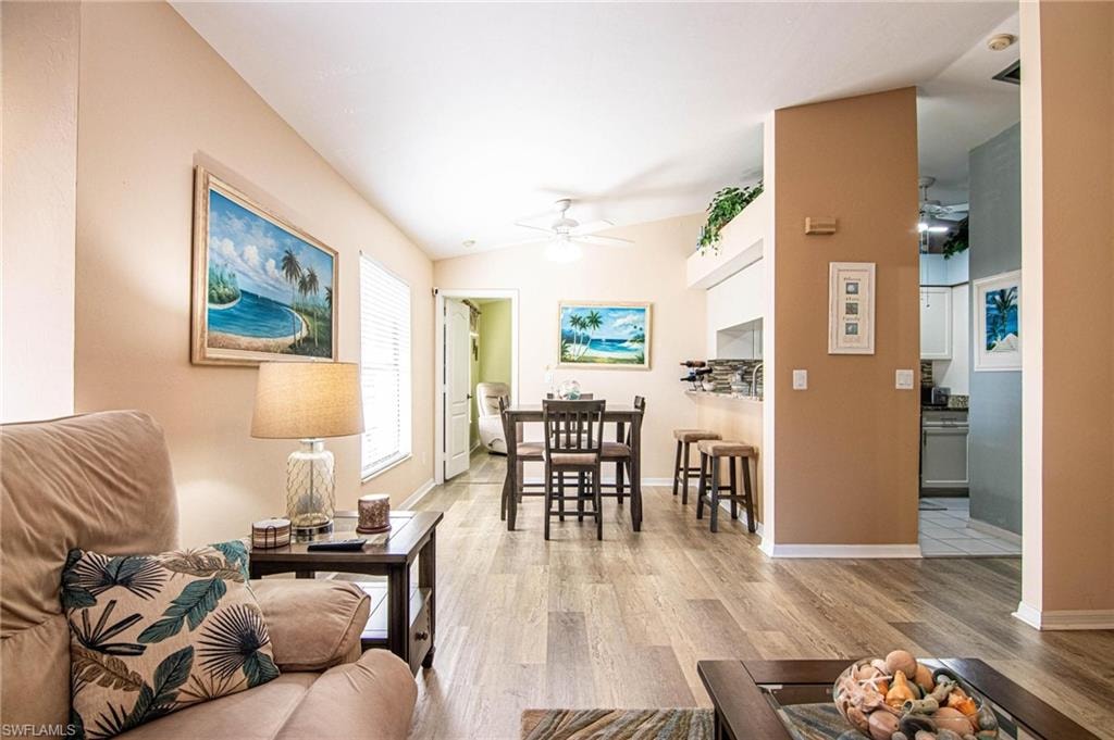 Living room with ceiling fan, light hardwood / wood-style floors, and vaulted ceiling