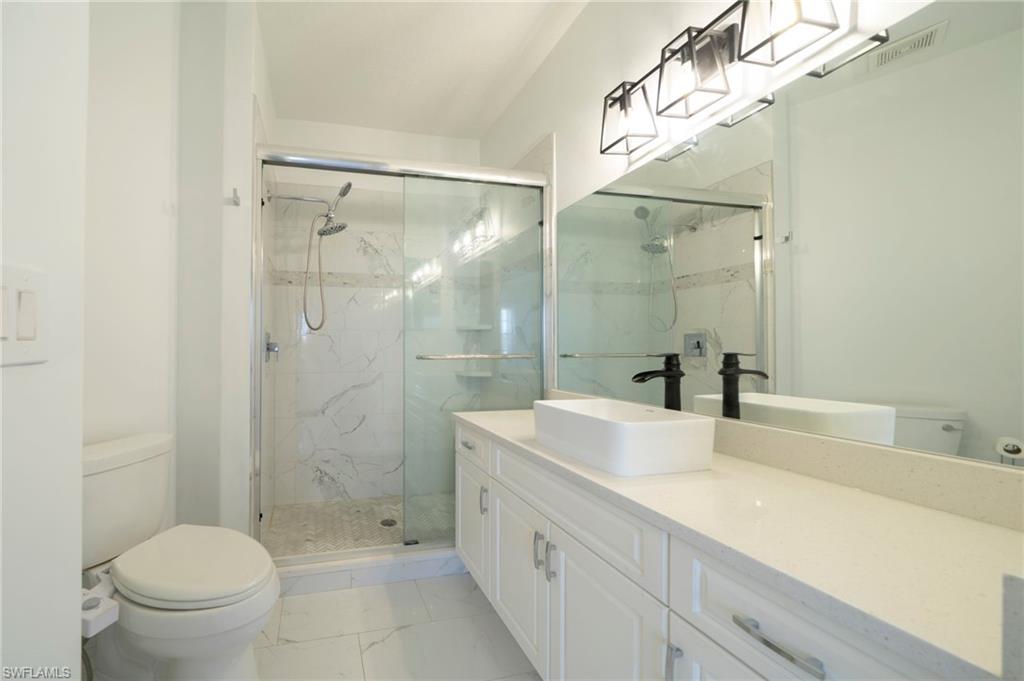 Bathroom featuring vanity, a marble finish shower, and light marble finish floors