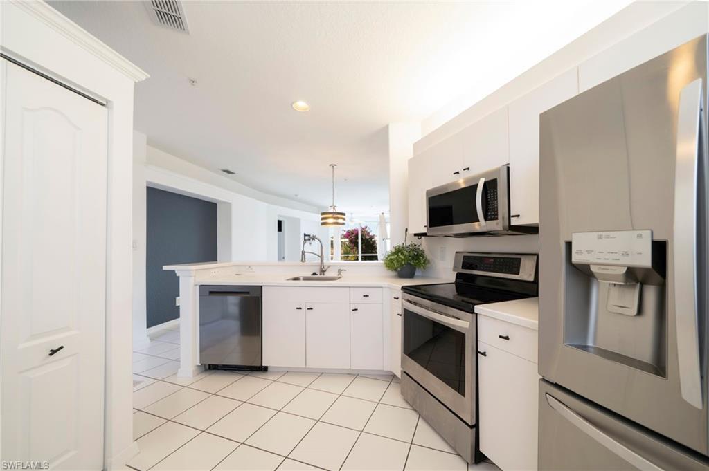 Kitchen with appliances with stainless steel finishes, a peninsula, light countertops, decorative light fixtures, and white cabinetry