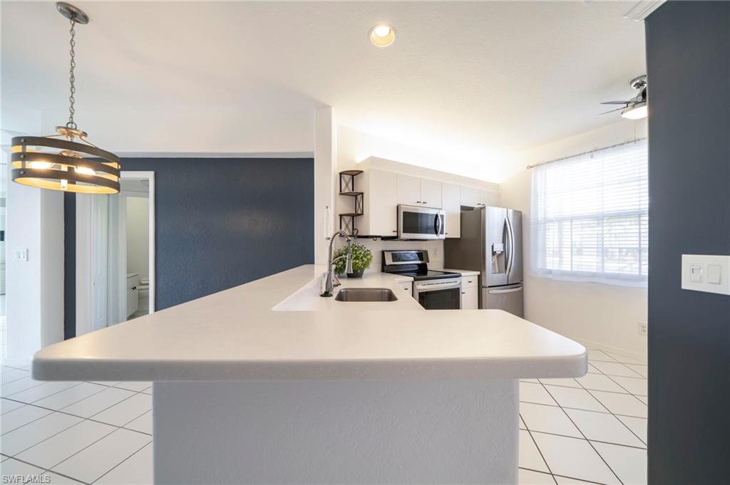 Kitchen with appliances with stainless steel finishes, a peninsula, light countertops, light tile patterned floors, and decorative light fixtures