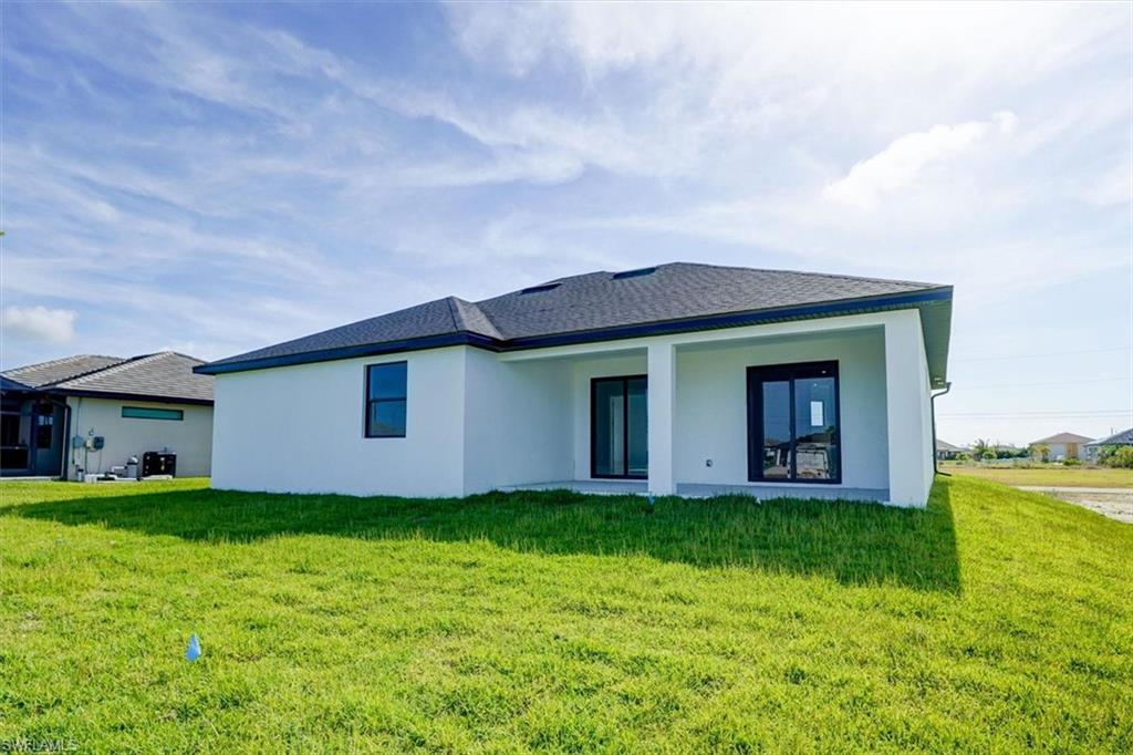 Rear view of house with stucco siding, a lawn, and a patio