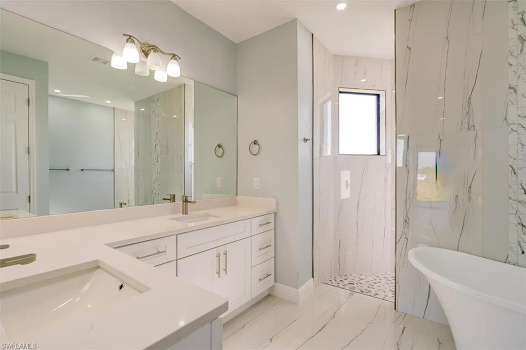 Full bath featuring a marble finish shower, double vanity, a freestanding tub, recessed lighting, and light marble finish floors