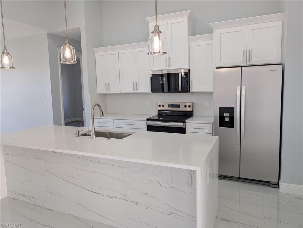 Kitchen featuring stainless steel appliances, light stone counters, white cabinets, decorative light fixtures, and a kitchen island with sink