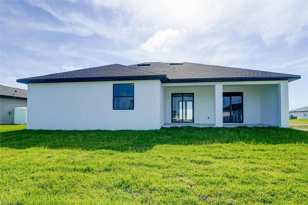 Rear view of property with a lawn, stucco siding, and a patio