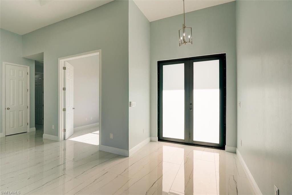 Entrance foyer with healthy amount of natural light, a towering ceiling, french doors, a chandelier, and light marble finish floors