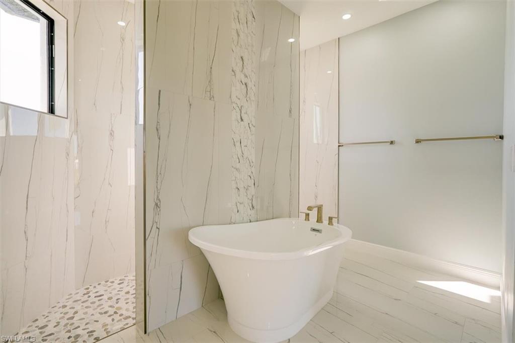 Full bath featuring stone wall, a freestanding tub, recessed lighting, a marble finish shower, and tile walls
