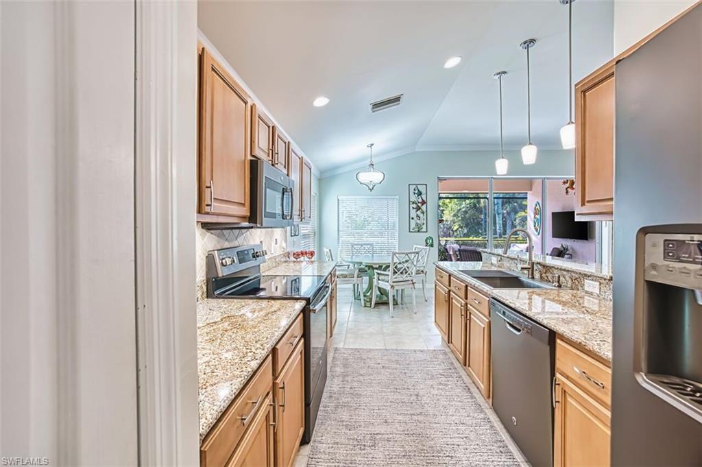 Kitchen featuring lofted ceiling, appliances with stainless steel finishes, decorative light fixtures, light stone countertops, and a peninsula