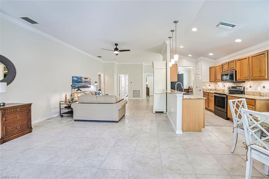 Kitchen with ornamental molding, light stone countertops, open floor plan, appliances with stainless steel finishes, and pendant lighting