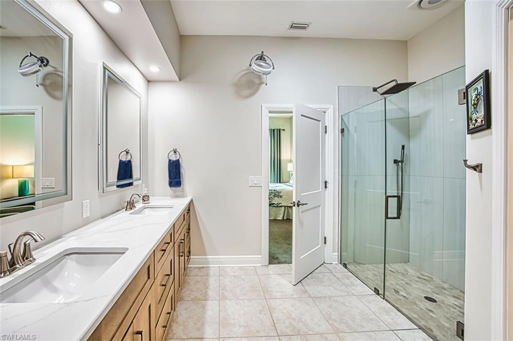 Ensuite bathroom with a shower stall, double vanity, light tile patterned flooring, and recessed lighting