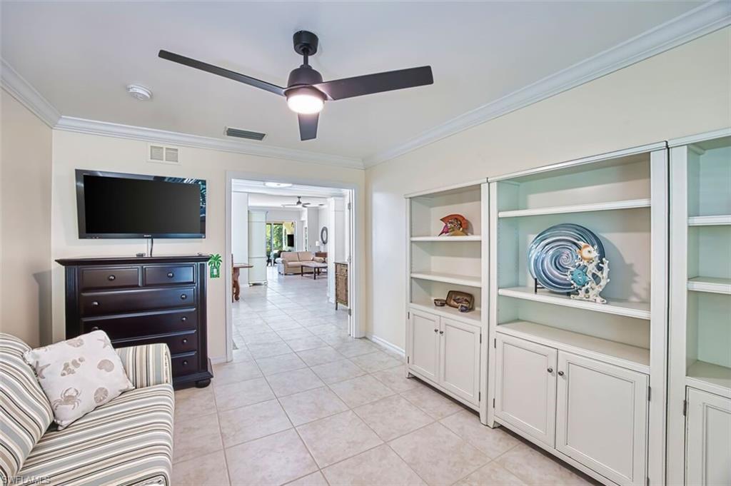 Living area with crown molding, light tile patterned floors, built in shelves, and ceiling fan