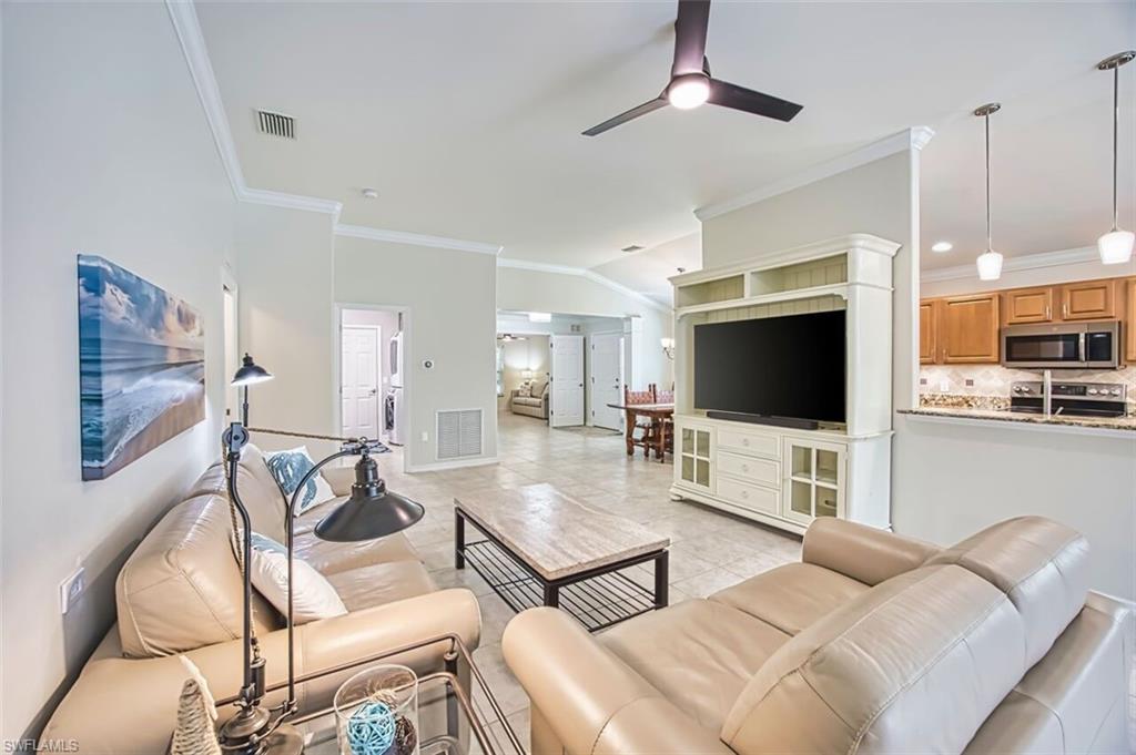 Living area featuring crown molding, vaulted ceiling, ceiling fan, and light tile patterned floors