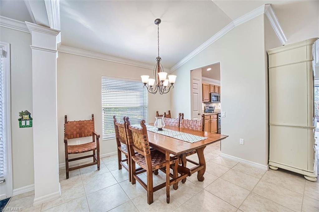 Dining area featuring lofted ceiling, crown molding, ornate columns, a chandelier, and light tile patterned floors