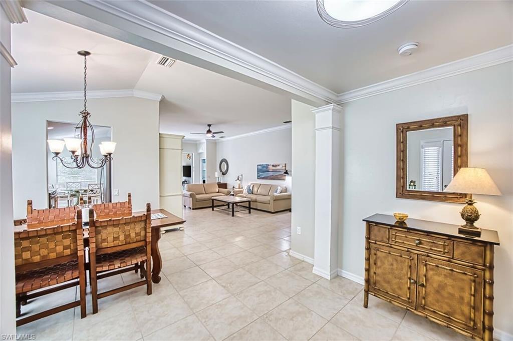 Dining area with ornamental molding, a chandelier, a ceiling fan, light tile patterned floors, and vaulted ceiling