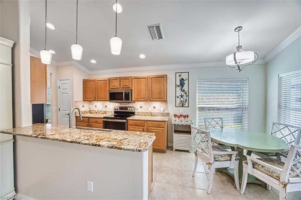 Kitchen featuring hanging light fixtures, light stone countertops, appliances with stainless steel finishes, tasteful backsplash, and brown cabinetry
