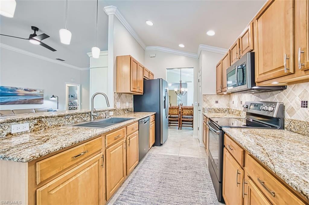 Kitchen featuring hanging light fixtures, appliances with stainless steel finishes, light stone countertops, crown molding, and ceiling fan