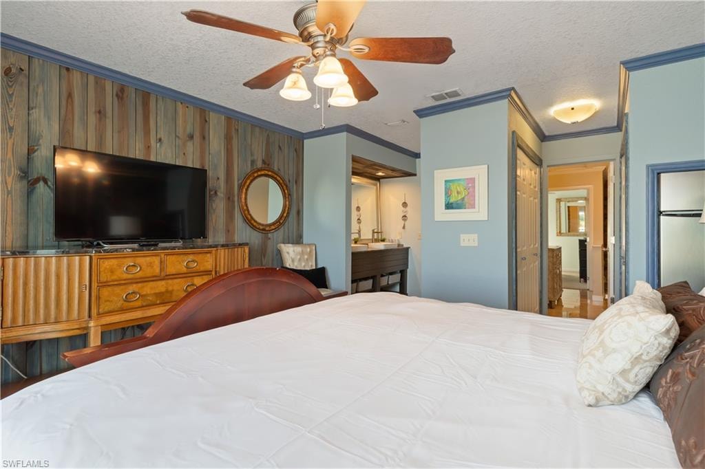 Bedroom with ornamental molding, a textured ceiling, a closet, a ceiling fan, and connected bathroom