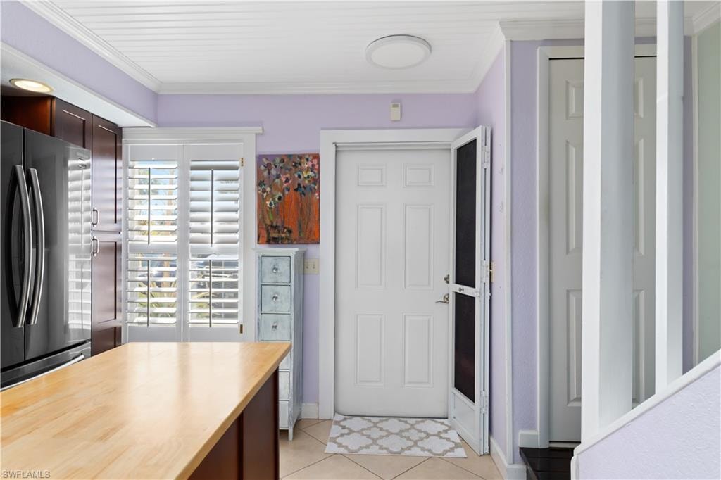 Kitchen featuring dark wood finish cabinets, freestanding refrigerator, light countertops, crown molding, and light tile patterned floors