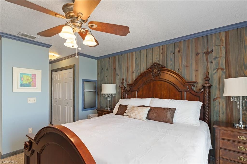 Bedroom with ornamental molding, a closet, a ceiling fan, a textured ceiling, and wooden walls
