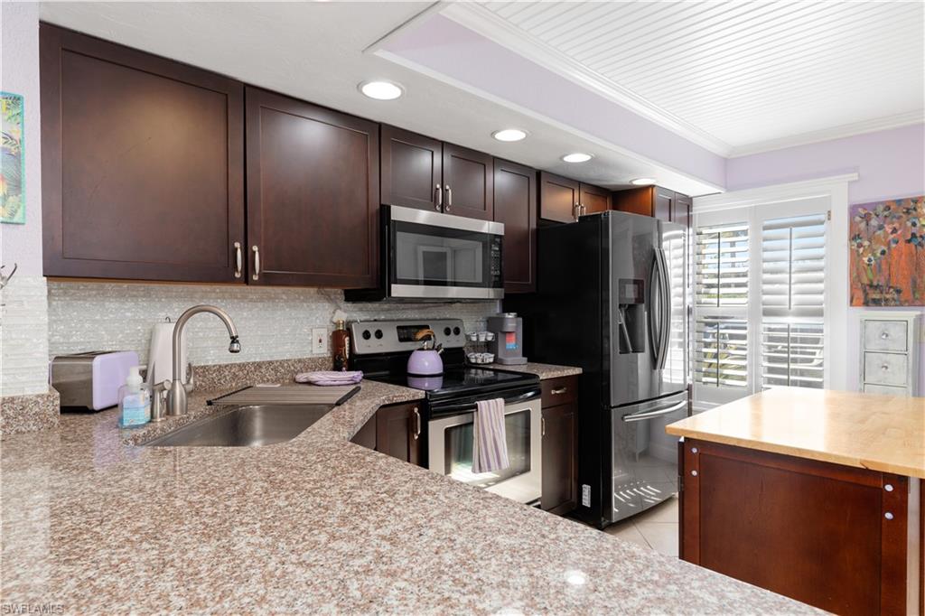 Kitchen with crown molding, stainless steel appliances, dark wood finish cabinetry, light stone countertops, and recessed lighting